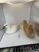 Two wooden duck decoys displayed side by side on white background, one natural wood tone and the other white painted