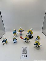 Nine vinyl Smurfs figurines arranged, showing various characters and activities, including tennis, ballet, and bandaged Smurf.