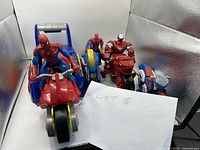 Front view of four motorcycles with action figures: Spider-Man on large red and blue spiked track motorcycle, smaller Spider-Man on blue and yellow bike, Iron Man on red motorcycle, and blue white red motorcycle without figure.