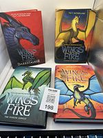 Four hardcover Wings of Fire books arranged showing cover art with dragons and titles including 'Darkstalker', 'The Dragonet Prophecy', 'The Poison Jungle', and 'The Lost Continent'.