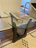 Side angle of table showing amoeba-shaped glass top on black wooden base with books