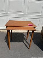 Two teak nesting tables nested in front of garage door on pavement