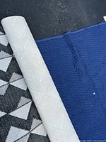 Photo of folded rug showing black and cream geometric diamond pattern and blue edging, alongside a blue fabric underneath.