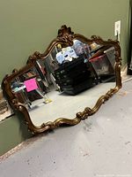 Front view of full mirror leaning against wall showing carved frame and glass surface.