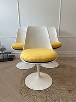 Three white tulip chairs with yellow cushions shown front view