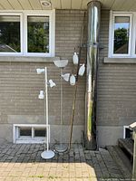 Overall view of three floor lamps side by side against a brick wall outside, showing size and style differences