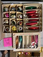 Top view of two cardboard trays showing 12 indented reflector ornaments, red and green elongated ornaments, and a retail box of 4 icicle shapes
