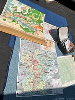 Photo showing large color-coded French map of Rhône-Alpes, laid flat and held by dowel, alongside other maps and storage case