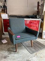 Front three-quarter view of the armchair showing teak arms, fabric color and tapered legs.