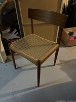 Front side view of mid-century wooden dining chair with cord seat showing the leg structure and seat detail.