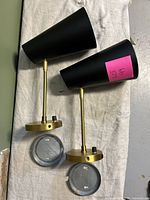Two mid-century modern black and gold wall sconces laid flat showing tops and undersides, with round mounting plates detached.