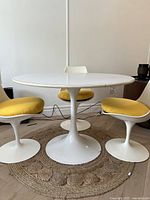 Front view of round table showing tabletop and pedestal base on jute rug with chairs in background