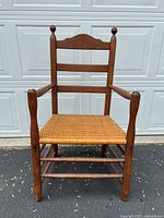 Front view of rustic antique wooden armchair with woven cane seat, showing curved backrest and arms.