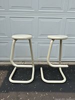 Two off-white Haworth K700 bar stools side by side on asphalt in front of garage door