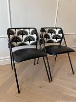 Front view of two retro metal dining chairs with black and white upholstered backs and black vinyl seats, showing overall condition and design.