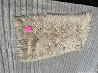 Top view of small cream colored shaggy Flokati rug laid on grey carpet, showing thick wool pile and rectangular shape.