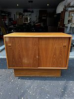 Front view of small teak cabinet showing two sliding doors and wood grain pattern.