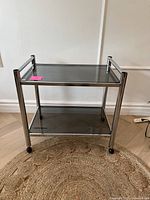 Full front view of tubular chrome bar cart showing both smoked glass shelves and caster wheels