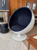 Front three-quarter view of white spherical ball chair with black cushions on pedestal base in living room setting.