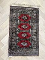 Full top-down view of rectangular vintage rug showing five red geometric medallions on a black and beige background with multiple intricate borders using black, white, and pink.