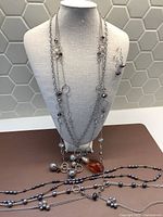 Photo showing multiple silver-tone chains with beads and large amber pendant, and matching bead earrings on display bust
