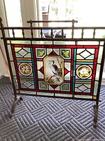Full frontal view of brass-framed stained glass fireplace screen on metal stand with finials