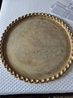 Full view of large round brass tray showing scalloped raised edge and engraved floral design on surface.
