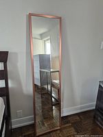 Front view of the tall rectangular IKEA Stave mirror with a thick copper-colored frame leaning against a wall in a room.