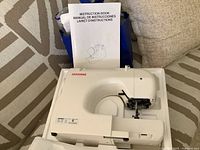 White Janome sewing machine in foam insert with instruction book propped behind