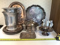 Photo showing assortment of vintage silverplated items including trays, ice buckets, lidded serving dish, compote, small tray, and porcelain salt and pepper shakers.