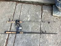 Two fishing rods with reels laid flat on stone surface, showing full rods with cork handles and reels attached.
