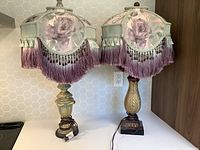 Two vintage-style table lamps with fabric rose print shades and fringed trim shown together on a countertop.
