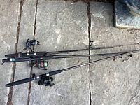 Three fishing rods laid on stone surface, showing rod length and attached reels