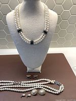 Photo showing two multi-strand faux pearl necklaces with green rectangular accent beads on a display bust, and two pairs of clip-on earrings in front of the bust.