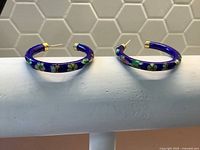 Pair of blue enameled cloisonné hoop earrings resting on a white surface.