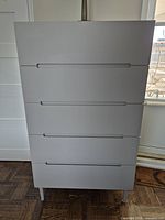 Front view of the modern tall gray dresser with five drawers, showing integrated handle grooves and smooth flat drawer fronts.