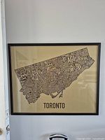 Photo of a modern styled framed city map of Toronto, showing word-based geographic layout in black text on beige background, brown plastic frame.