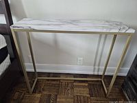 Front view of the console table showing white faux marble top and gold metal frame on wooden floor.