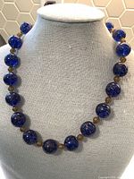 Front view of the necklace displayed on a beige mannequin bust showing the blue and gold glass beads.
