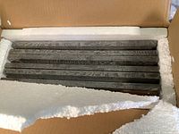 Box containing 7 grey wood grain textured picture frames, stacked horizontally with styrofoam protection.