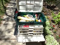 Opened Plano fishing tackle box showing upper compartments with various fishing gear inside, including bobbers and line spool