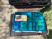 Two stacked fishing tackle boxes outdoors with a black base and translucent blue lid showing internal compartments.