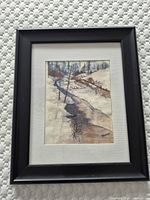 Framed watercolor painting of a winter river landscape seen from above, showing the entire frame and matting.