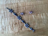 Set of sterling silver bracelet with purple gemstone flowers and matching flower earrings on wood grain surface.