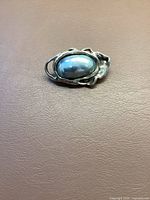 Full view of abalone silver brooch on brown surface showing shell and silver details