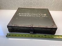 Metal ammo box with stenciled text and rusted metal corners, showing measurement tape indicating width around 14 inches.