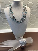Full view of the multi-strand fish necklace with turquoise beads on display stand and the wide silver cuff bracelet on a mannequin hand.