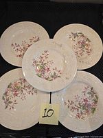 Five 10-inch plates with floral motifs and embossed rims arranged on a black surface.