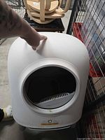 White dome-shaped automatic cat litter box with front circular opening showing interior scoop and handle on top.