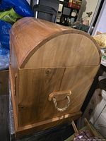 Side view of the cedar chest showing wood grain, rope handle, and rounded top shape.